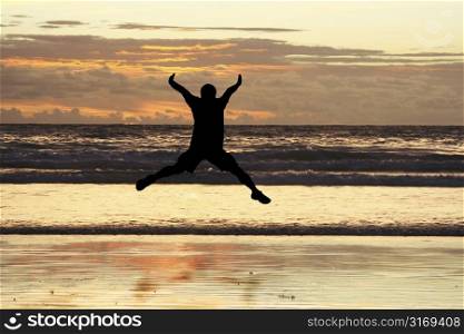 A man jumping on the beach showing happiness (in silhouette)