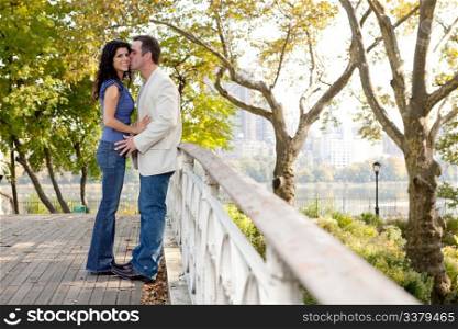 A man kissing a woman in a park on a bridge