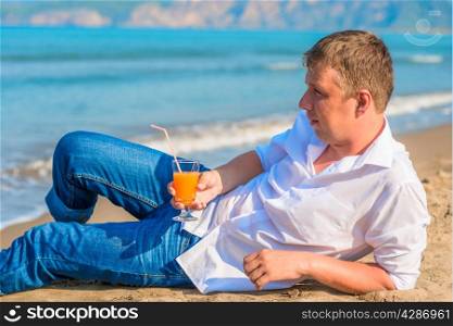 a man lies with a cocktail on the sandy beach in clothes