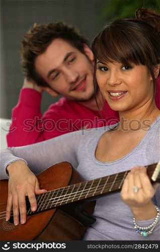 a man looking a woman playing guitar