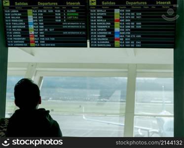 A man looking at information departure board and checking his flight in the airport for travel in Europe. Passenger looking timetable digital display at airport terminal. Tourist with delay flight.