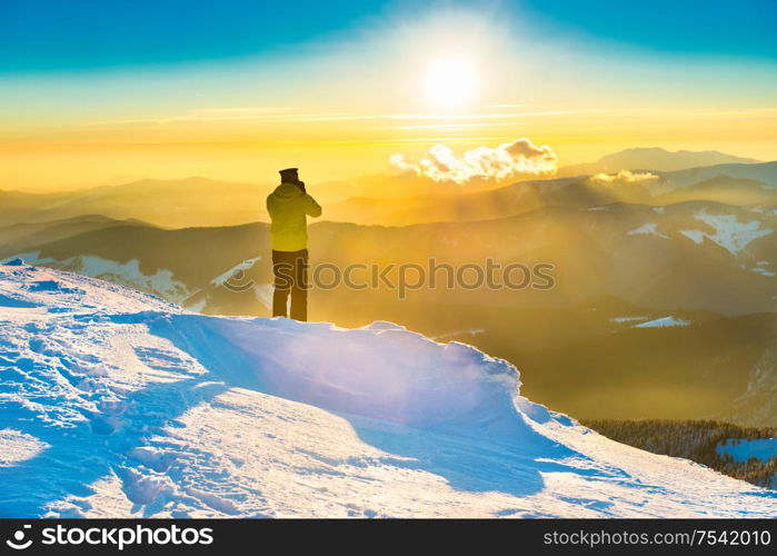 A man looking at sun and beautiful sunset in winter mountains with snow