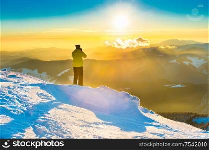 A man looking at sun and beautiful sunset in winter mountains with snow