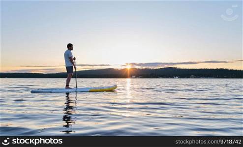 A man on a paddle board in the rays of the setting sun.. A man on a paddle board in the rays of sun.