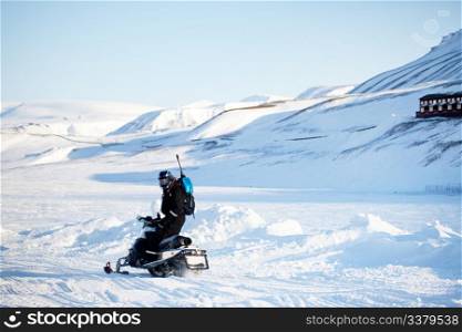 A man on a snowmobile with a gun and shovel for safety
