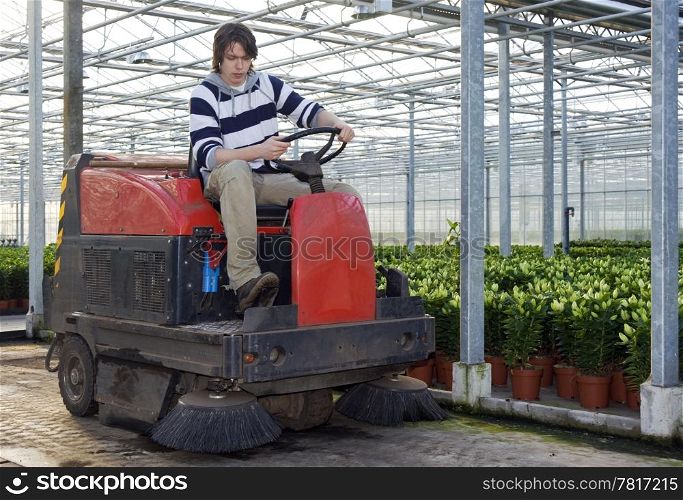 A man on an industrial cleaning machine, cleaning the concrete floor of a glasshouse