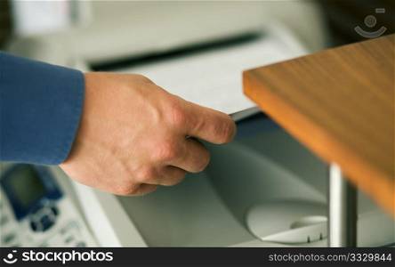 A man (only hand to be seen) faxing documents or taking them out of a printer