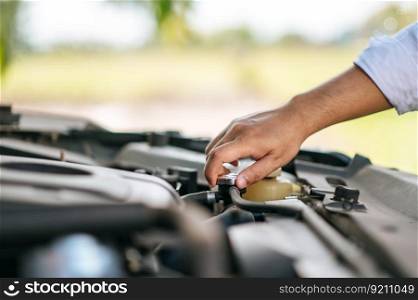 A man opens the hood of a car to repair the car due to a breakdown.