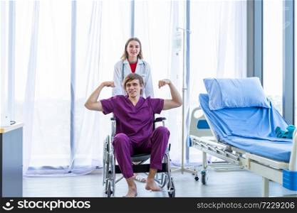 a man patient sit in a wheelchair show showing thumbs up with smiley face very good symptom and female doctor therapeutic advising with positive emotions in hospital background.