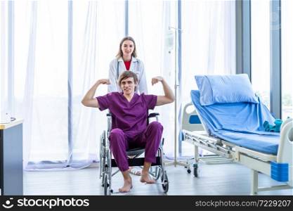 a man patient sit in a wheelchair show showing thumbs up with smiley face very good symptom and female doctor therapeutic advising with positive emotions in hospital background.