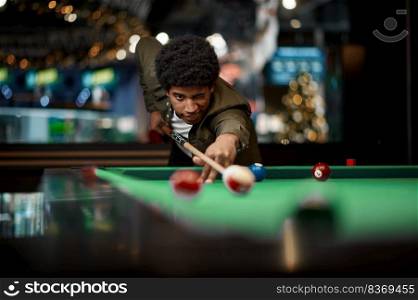 A man playing billiard, focus on serious concentrated face of pool player aiming ball with cue. Portrait of man playing billiard