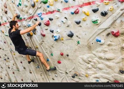 A Man practicing rock climbing on artificial wall indoors. Active lifestyle and bouldering concept.