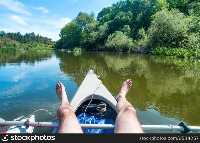 A man relaxing on kayak at the river. Landscape with blue water and green trees. A man relaxing on kayak