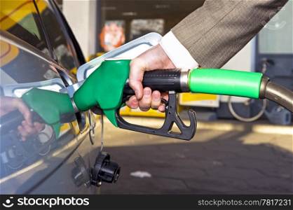 A man&rsquo;s hand filling up a car with gas or petrol at a gas station.