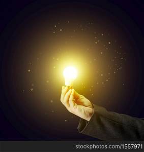 a man&rsquo;s hand holds a glass lamp on a dark background. Concept of new ideas, brainstorming, innovation