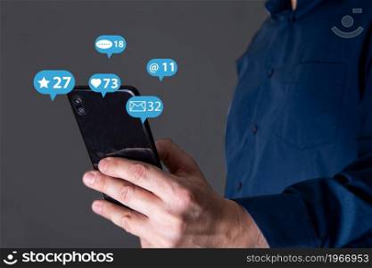 A man&rsquo;s hand holds a phone, icons of messages from social networks. The concept of using the phone.. A man&rsquo;s hand holds a phone, icons of messages from social networks.