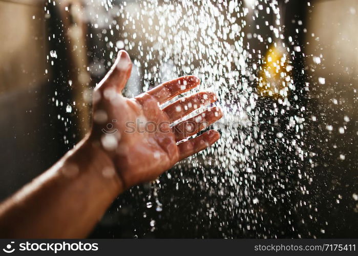 A man&rsquo;s hand in a spray of water in the sunlight against a dark background. Water as a symbol of purity and life.. A man&rsquo;s hand in a spray of water in the sunlight against a dark background. Water as a symbol of purity and life