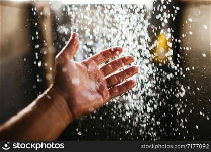 A man&rsquo;s hand in a spray of water in the sunlight against a dark background. Water as a symbol of purity and life.. A man&rsquo;s hand in a spray of water in the sunlight against a dark background. Water as a symbol of purity and life