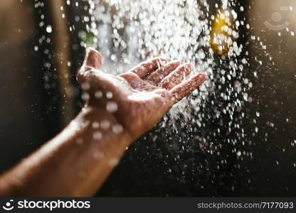 A man&rsquo;s hand in a spray of water in the sunlight against a dark background. Water as a symbol of purity and life.. A man&rsquo;s hand in a spray of water in the sunlight against a dark background. Water as a symbol of purity and life