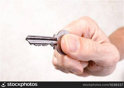 A man&rsquo;s hand is holding a key, opening or closing a door, on light background