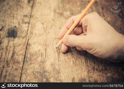 A man&rsquo;s hand is writing on atable with a pencil