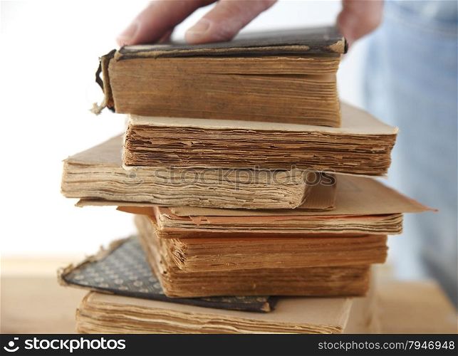 a man&rsquo;s hand on a stack of old books