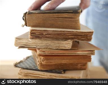 a man&rsquo;s hand on a stack of old books