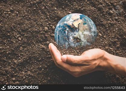 A man&rsquo;s hand wraps around a small world on the ground, environmental concepts, Element of image furnished by NASA.