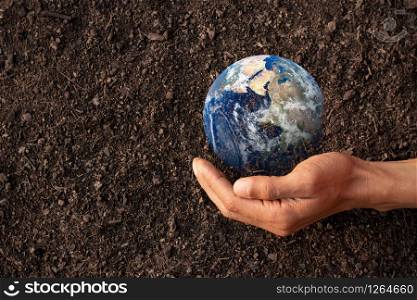 A man&rsquo;s hand wraps around a small world on the ground, environmental concepts, Element of image furnished by NASA.