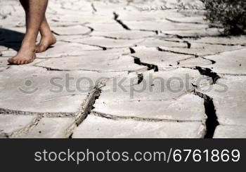 A man`s feet on dry, cracked desert earth