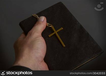 a man?s hand holds a bible in a dark binder a metal cross on a chain close-up. hand holds the cross and Biblie. hand holds the cross and Biblie