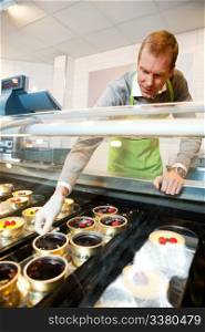 A man selling gourmet deserts from behind a glass counter