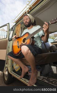 A man sits with his guitar and sigarette in hand inside his classic combi van