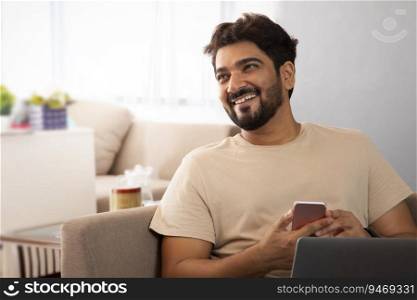 A man sitting with laptop holding his mobile looking sideways.