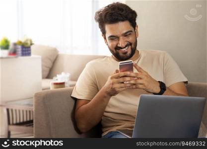 A man sitting with laptop smiling while working on his mobile.