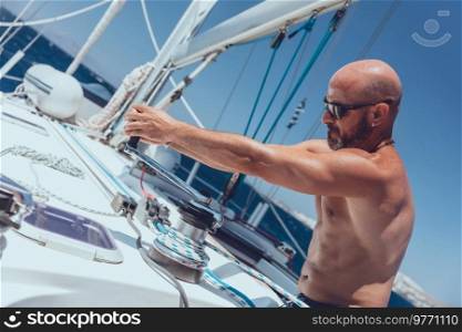 A man skipper tightens the cord onto the winch on a yacht. Opens the sail. Crew working on sailboat board. Vacation on the sea.. Experienced and strong Captain on solo sail