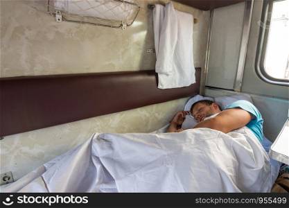 A man sleeps on the bottom shelf in a train car
