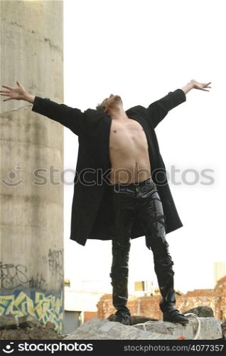a man standing on top of a pile of rubble rejoicing raising his arms into the sky.
