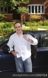 A man standing outside leaning on his car in front of his house