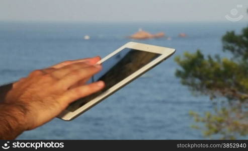 A man surfing the net with his iPad.Two hands touching the tablet screen and browsing.Leisure time touching iPad in the seashore.