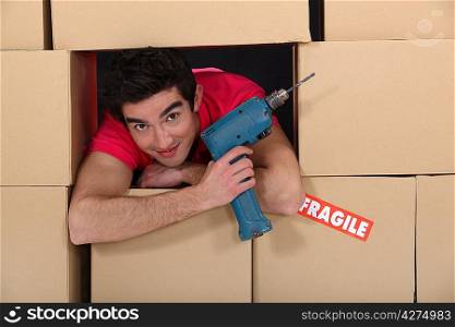 A man through a pile of cardboard boxes with a drill.