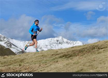 A man trains for ultra run trail on hilly meadow in autumn with the first snow on the mountains