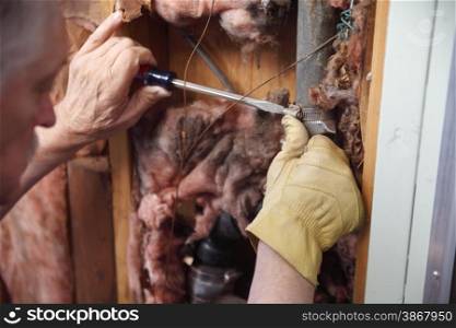 A man tries to repair a broken pipe in his house wall.