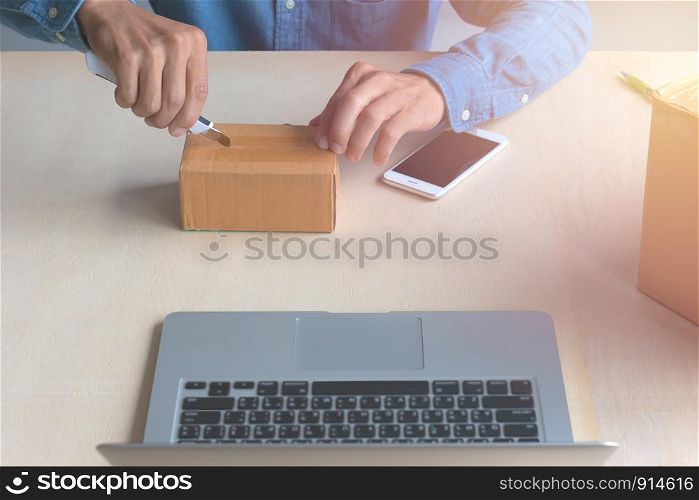 A man used a knife to open the product packaging box online on a wooden table.
