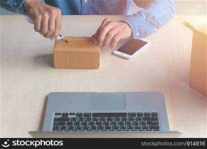 A man used a knife to open the product packaging box online on a wooden table.