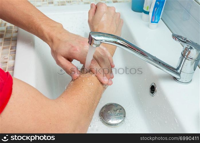 A man washes his hands up to the elbows under the tap