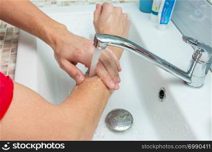 A man washes his hands up to the elbows under the tap