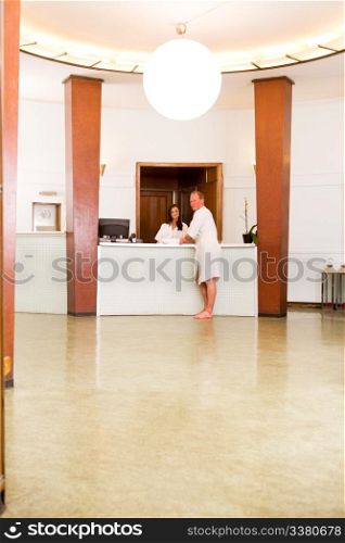 A man wearing a bathrobe standing in a spa reception with worker