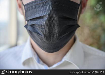 A man wearing a black respiratory mask on his face.. A man wearing a black respiratory mask on his face
