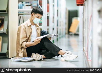 A man wearing masks is sitting reading a book in the library.